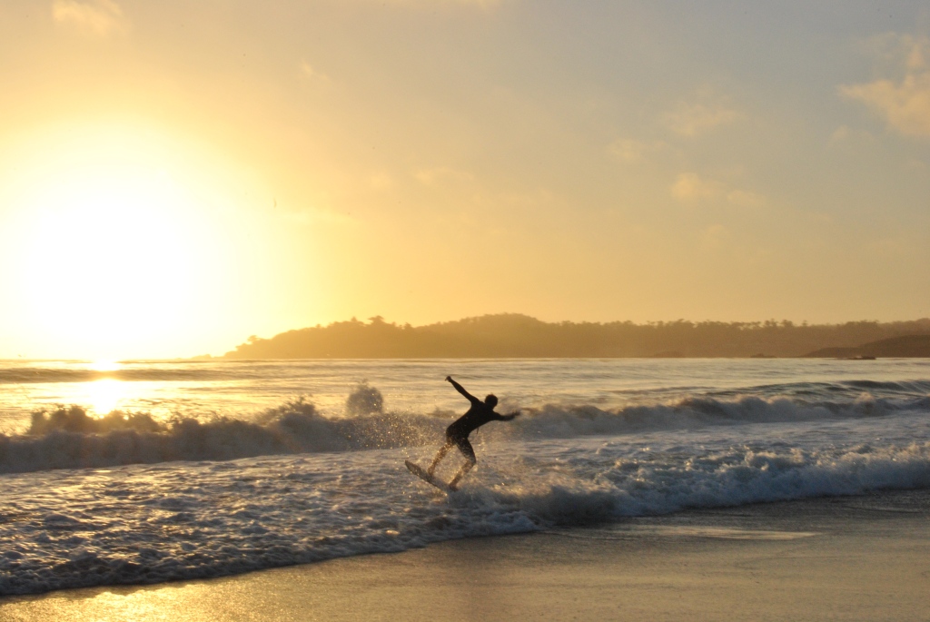 A skim boarder on a beach at sunset